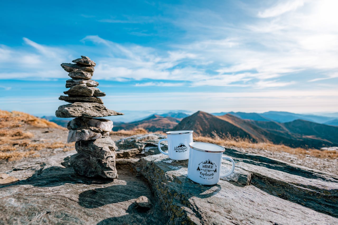 Serene mountain view with rock stack and mugs in Pietrosu, Romania.